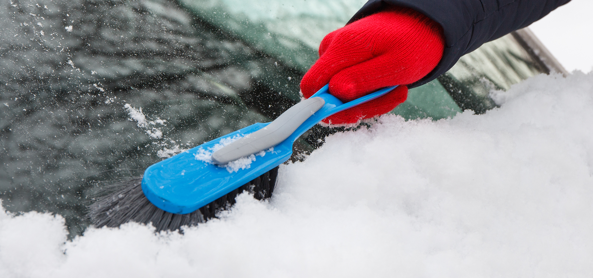 hand with a snow scrapper cleaning off a car window
